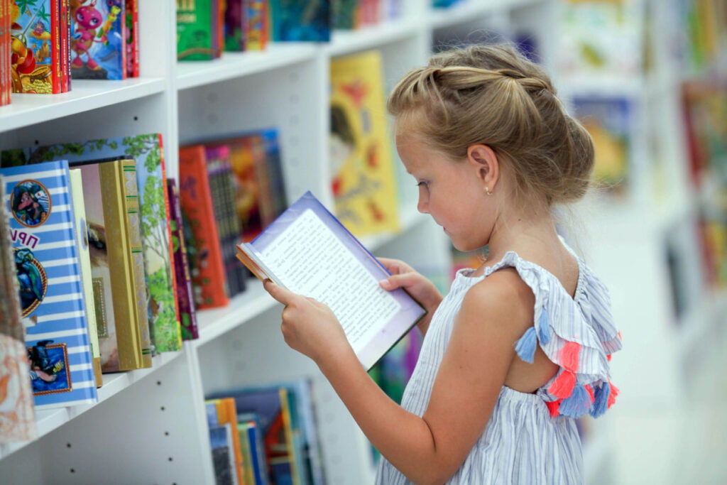 Une petite fille se tient dans une librairie et lit