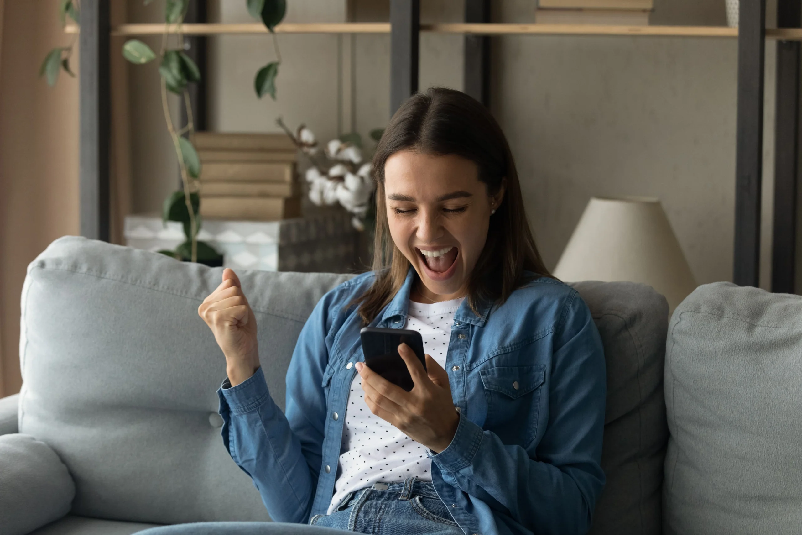 Une personne joyeuse s'assoit dans le salon avec un téléphone en main