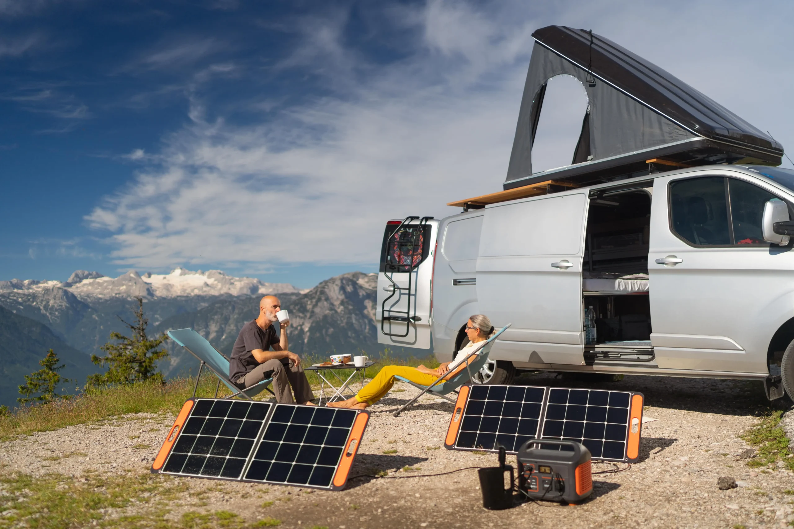 Un couple en camping recharge sa station électrique portable à l’aide d’un panneau solaire