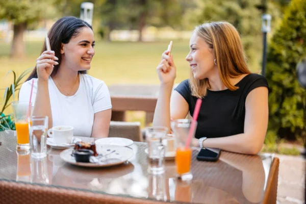 Deux femmes souriantes se détendent à l'extérieur d'un café, une vape à la main