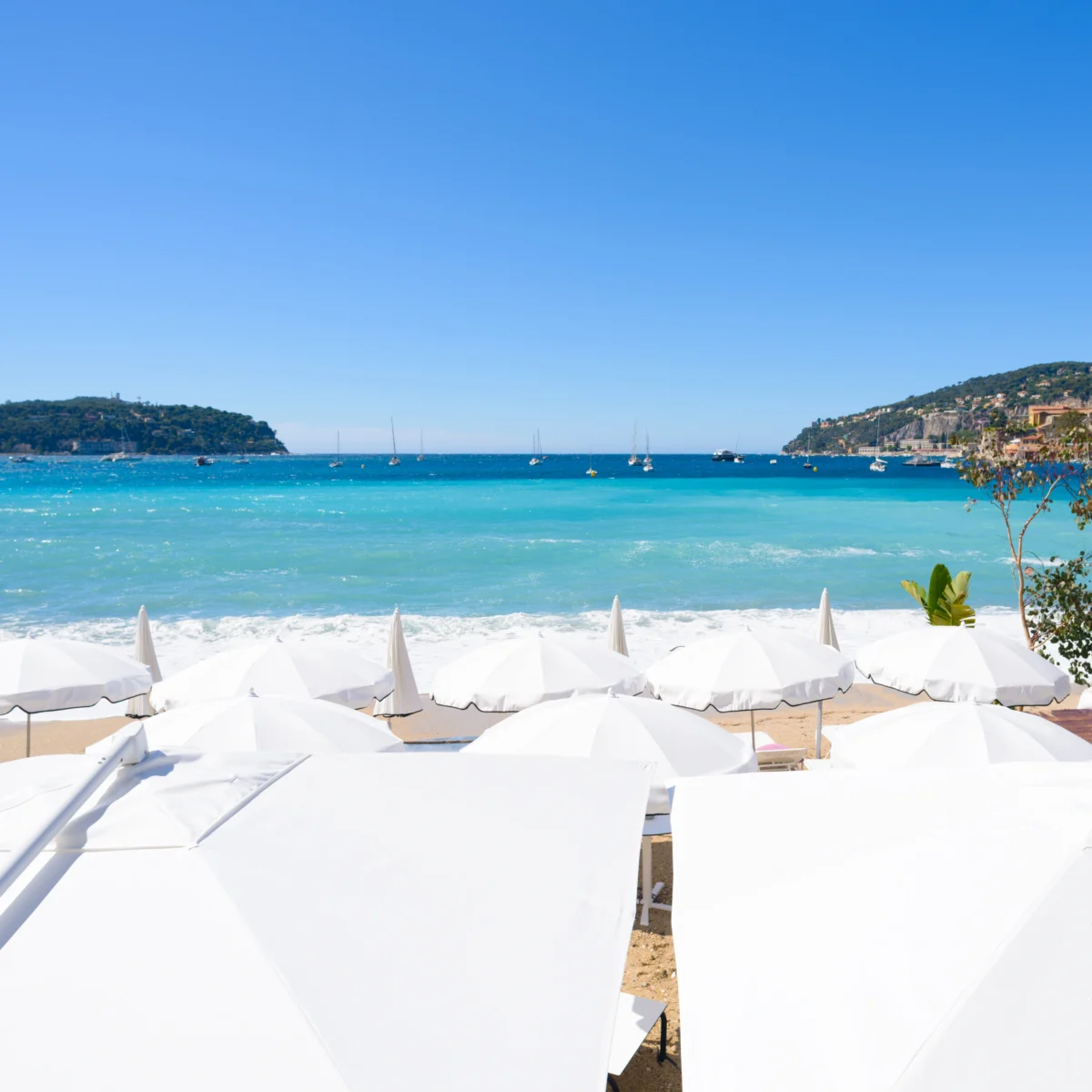 Une plage de la Côte d'Azur avec des parasols blancs, bordée par une mer turquoise.