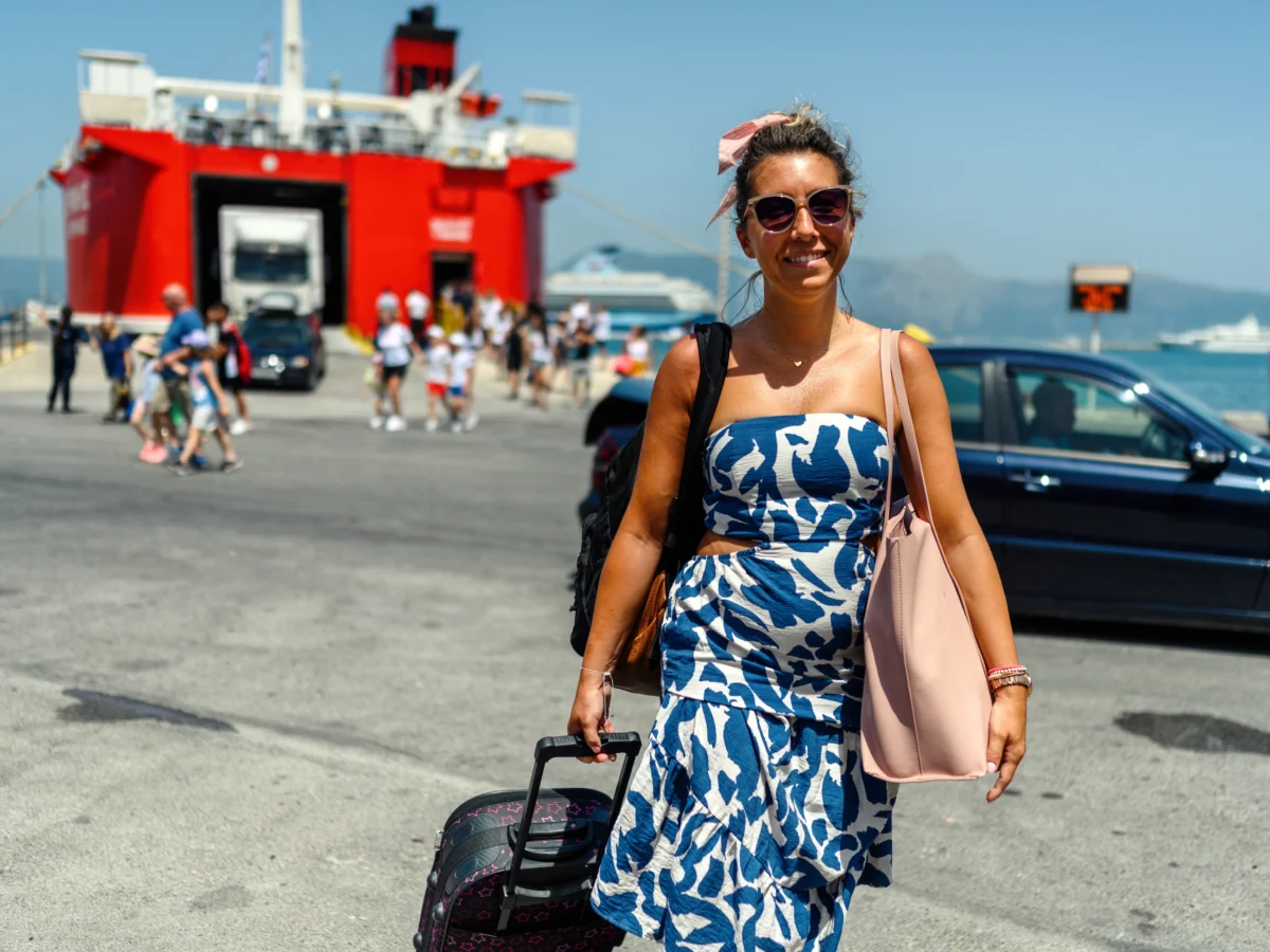 Une femme devant l'embarquement d'un ferry, valise à la main et sac à dos sur l'épaule droite